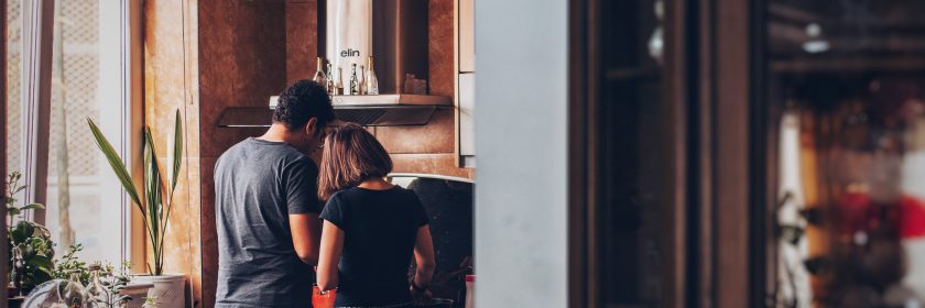 A young couple stand next to each other in their kitchen, cooking something together in their home.