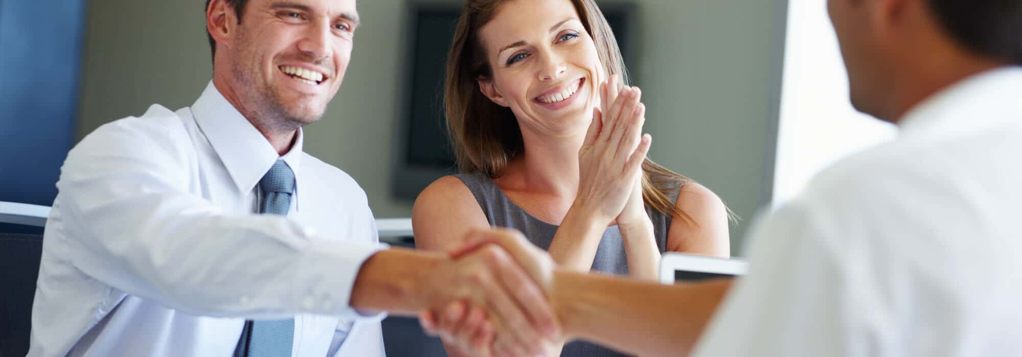 Young man and woman smiling and shaking the hand of a businessman