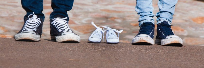 Photo of two parent's sneakers with an pair of baby shoes in the middle
