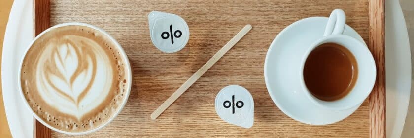 wooden tray with a cup of espresso and a cappuccino with creamers in the shape of percentage sign