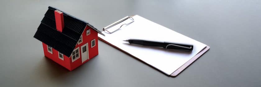 Miniature toy house next to a clipboard and pen
