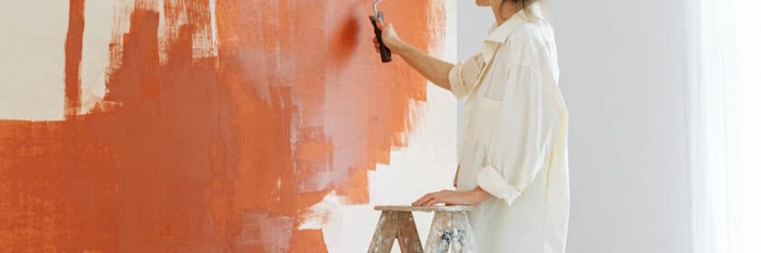 Woman on a ladder painting a room orange