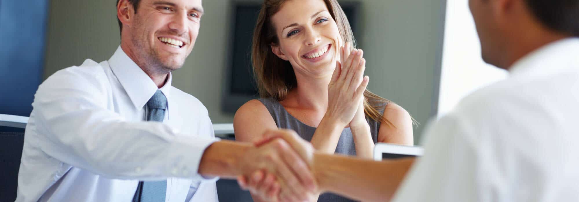 A man and woman sitting across from a business professional smiling and shaking hands