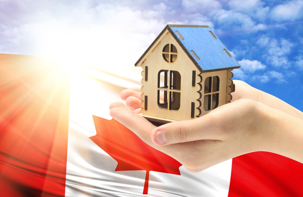 Hands holding a house with a Canadian flag in the background.