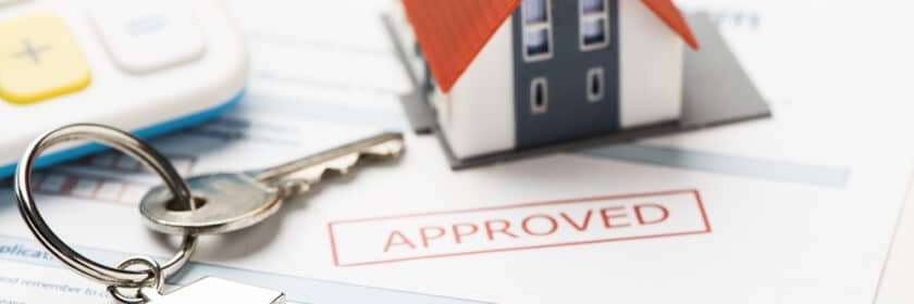 Mortgage approval papers with keys and a mini house on top.