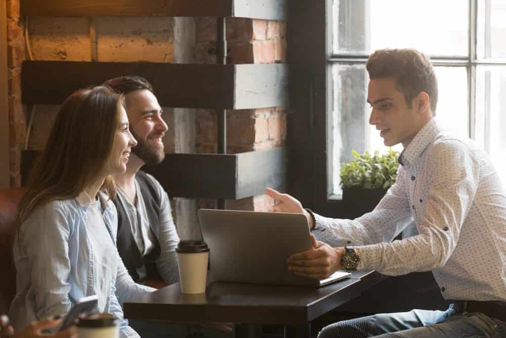 Man consulting young couple at coffeehouse with a computer