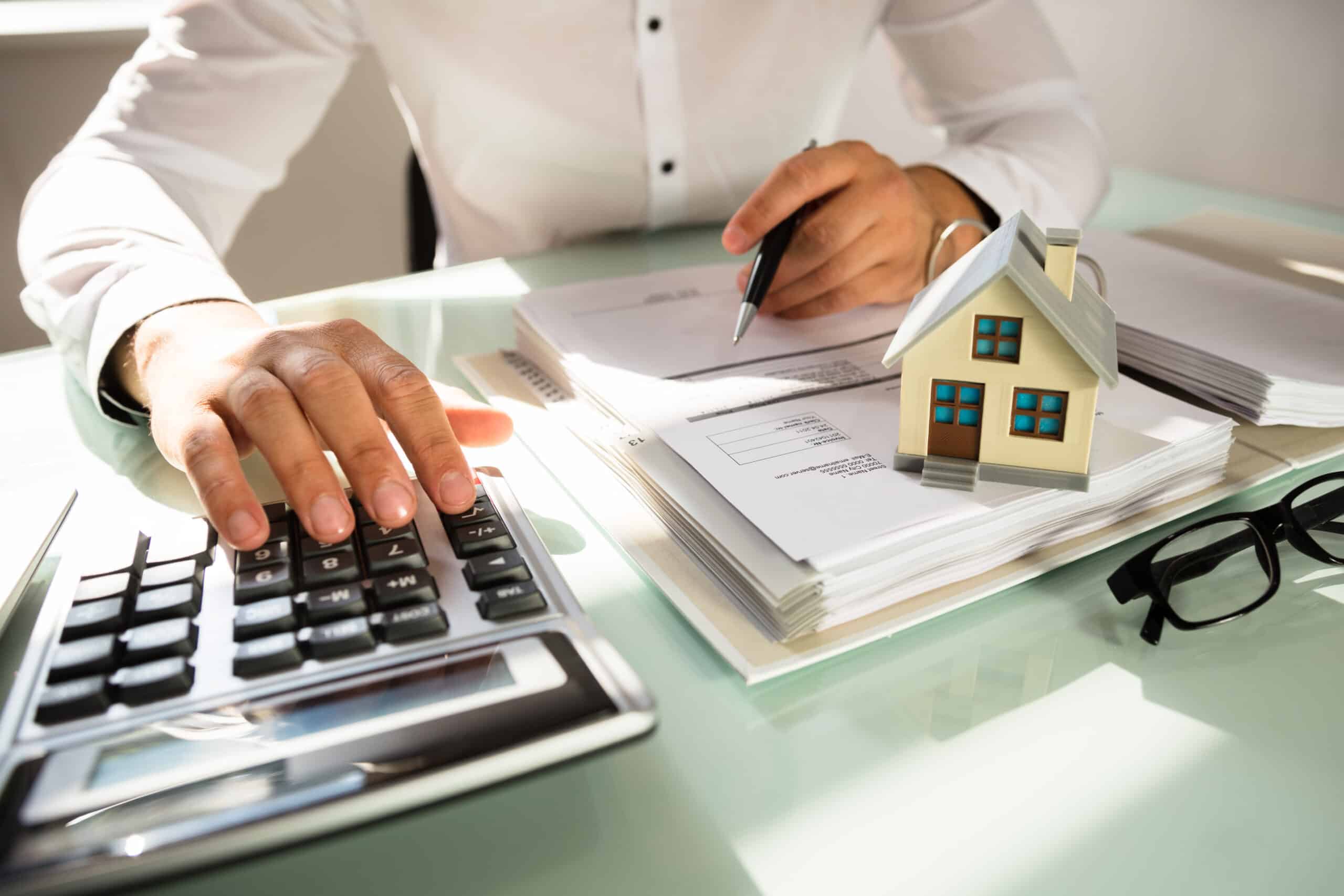 Businessman's,Hand,Calculating,Invoice,With,House,Model,In,Office